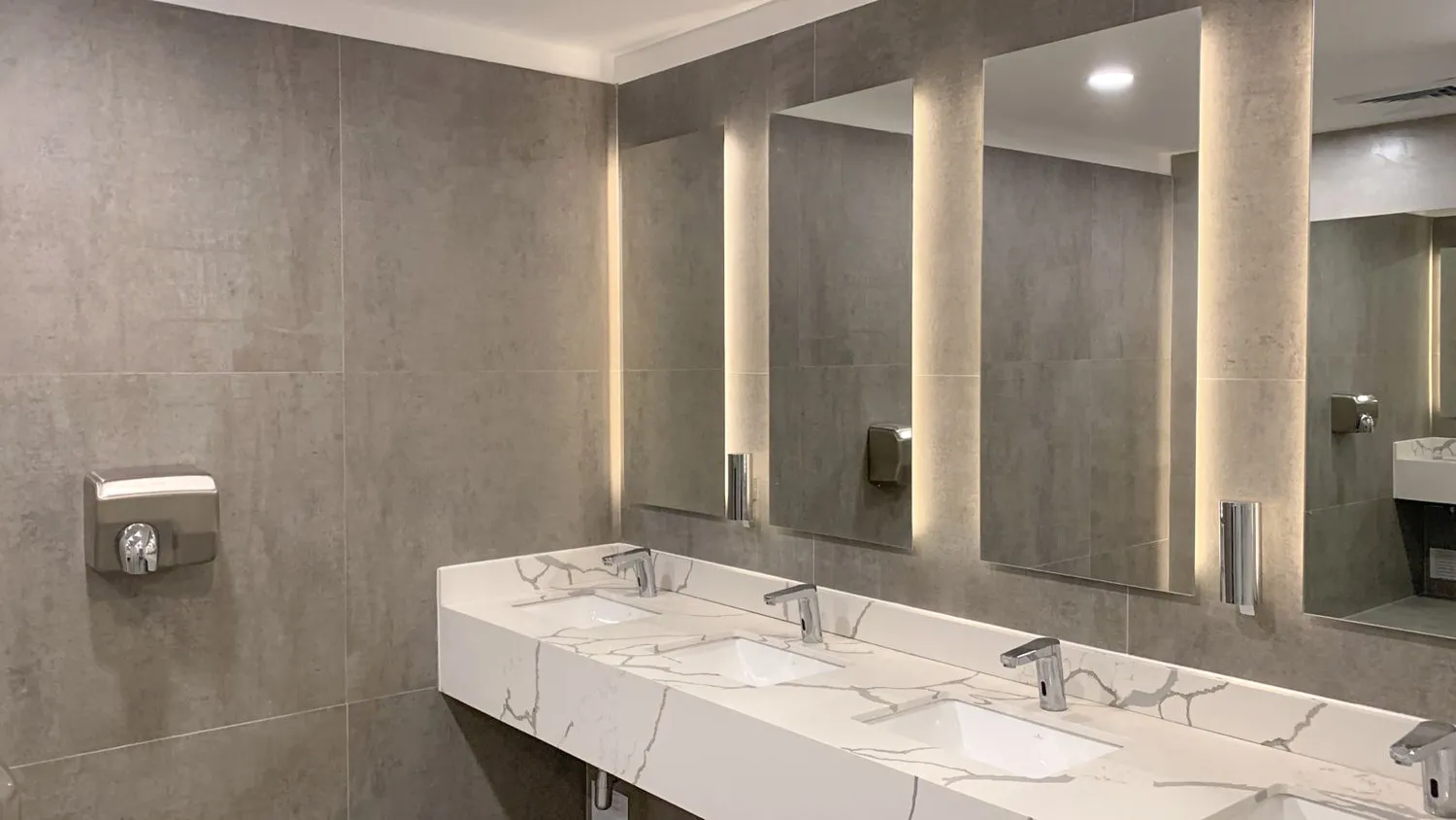 Baño corporativo con lavamanos corrido y espejos iluminados